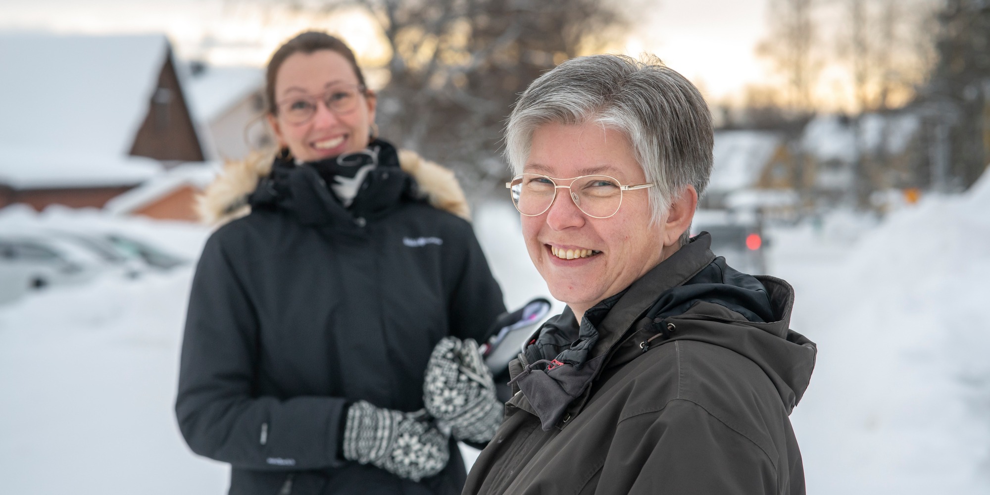 Två leende kvinnor står ute i snölandskap.
