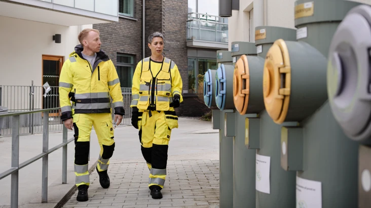 Två kollegor i gula varselkläder inspekterar tillsammans en rad sopnedkast.